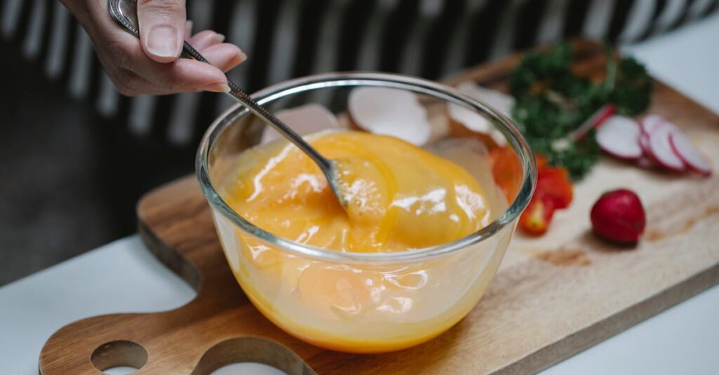 Hand whisking eggs in a bowl with fresh vegetables on a chopping board.